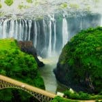 Aerial view of a waterfall cascading down a cliff with lush green surroundings. A bridge crosses the river at the base, surrounded by vibrant greenery. The scene is vibrant and dynamic, showcasing the waterfalls power and beauty.